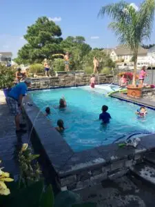A busy residential gunite swimming pool featuring a raised stone wall with multiple sheer descent water features and children playing in the water.
