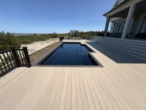 A luxury rectangular fiberglass inground swimming pool integrated into a premium light-colored composite deck, overlooking a scenic beach and bay.