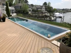 A luxury custom gunite inground swimming pool featuring extreme rubber surfacing coping and a light-colored wood deck, overlooking a scenic bay with boats.