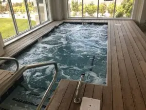 A luxury commercial gunite spa with bubbling water, integrated into a premium Ipe wood deck with stainless steel handrails.