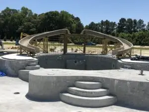 A gunite swimming pool under construction featuring a deep diving well, curved concrete steps, and two large custom slides positioned for future RicoRock masonry.