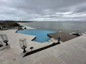 A luxury custom gunite inground swimming pool elevated 18 feet in the air with a vanishing edge overlooking the bay, featuring premium stone decking and modern outdoor lighting.