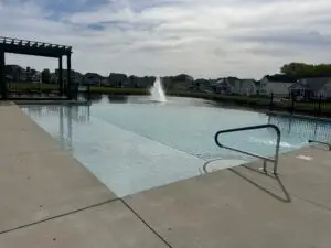 A large commercial gunite inground swimming pool featuring a vanishing edge (infinity edge) that overlooks a scenic lake with a fountain.