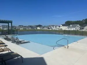 A large commercial gunite inground swimming pool featuring a vanishing edge (infinity edge) that overlooks a scenic pond and fountain, surrounded by a concrete patio with lounge chairs.