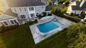 An aerial view of a custom rectangular gunite swimming pool with an integrated raised spillover gunite spa and a large stone paver patio.